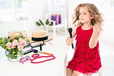 A little girl with cosmetics. She is in mothers bedroom, sitting near the mirror.の写真素材