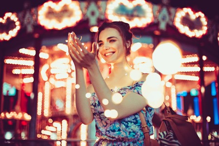 Beautiful young woman smiling and talking garlands of lights at cityの写真素材