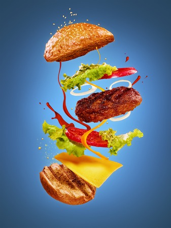 The hamburger with flying ingredients on blue background. Advertising conceptの写真素材