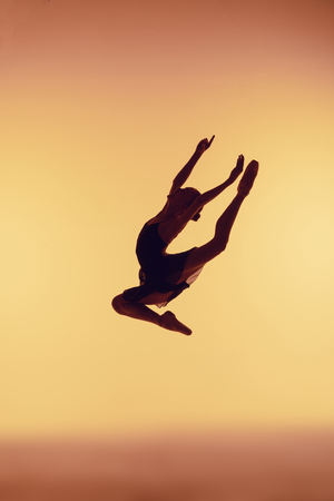 Beautiful young ballet dancer jumping on a orange background.の写真素材