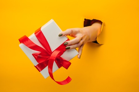 close-up of female hand holding a present through a torn paper, isolatedの写真素材