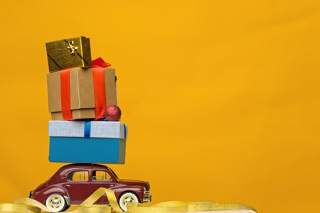 Blue retro toy car delivering Christmas or New Year gifts, on yellowの写真素材