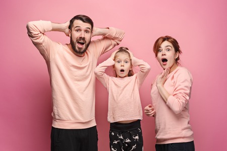 Surprised young family looking at camera on pinkの写真素材