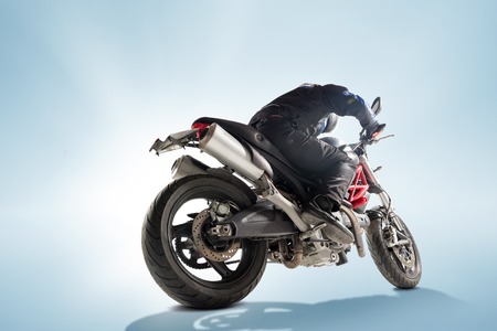 Biker in black jacket and helmet sitting on his sportive bike on blue backgroundの写真素材