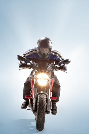 Biker in black jacket and helmet sitting on his sportive bike on blue background