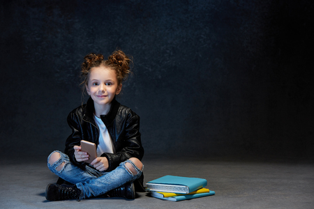 Little girl sitting with smartphone in studioの写真素材