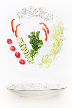 The salad bowl in flight with vegetables: tomato, cucumber, cabbage on white backgroundの写真素材