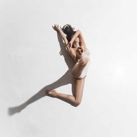 Young beautiful dancer in beige dress dancing on gray backgroundの写真素材