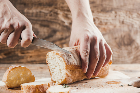 Whole grain bread put on kitchen wood plate with a chef holding gold knife for cut.