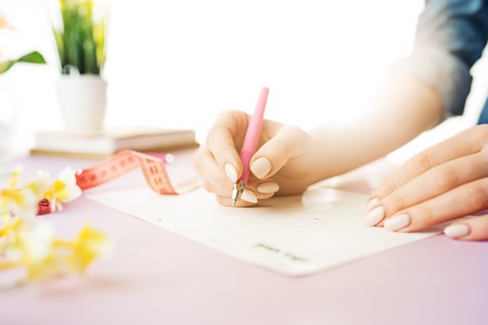 The female hands holding pen. The trendy pink desk.