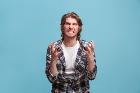 Portrait of an angry man looking at camera isolated on a blue backgroundの写真素材