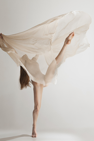 Young beautiful dancer in beige swimsuit dancing on gray backgroundの写真素材
