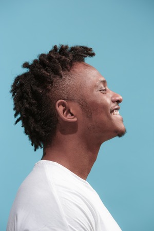 The happy business Afro-American man standing and smiling against blue background. Profile view.の写真素材