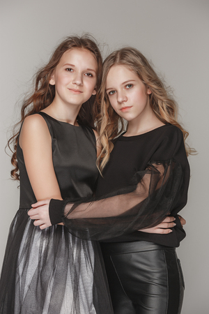 The fashion girls standing together and looking at camera over gray studio backgroundの写真素材