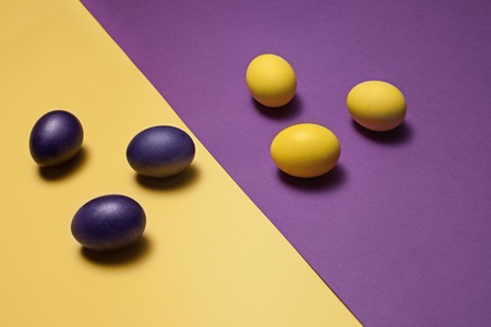 Beautiful easter table setting composition. A row of lilac and yellow color eggs on violet and yellow background. Happy Easter greeting card. Top view, copy space.の写真素材