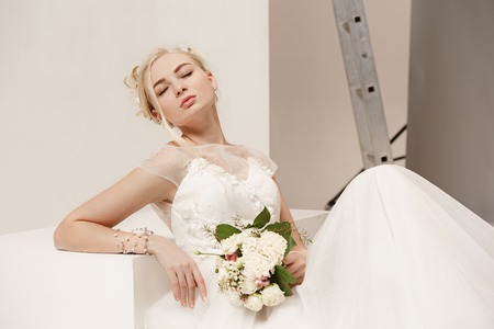 Bride in beautiful dress standing indoors in white studio interior like at home. Trendy wedding style shot. Young attractive caucasian model like a bride tender looking.の写真素材