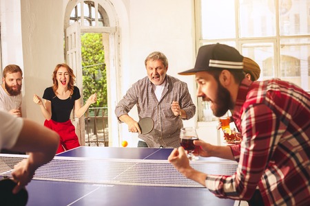 Group of happy young friends playing ping pong table tennis