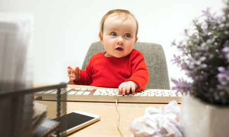 Happy child baby girl toddler sitting with keyboard of computer isolated on a white backgroundの写真素材