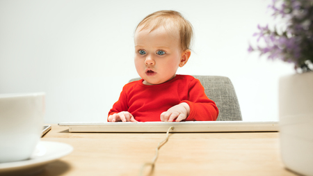 Happy child baby girl toddler sitting with keyboard of computer isolated on a white backgroundの写真素材