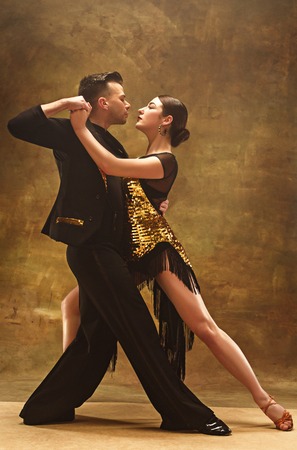 Dance ballroom couple in gold dress dancing on studio background.の写真素材