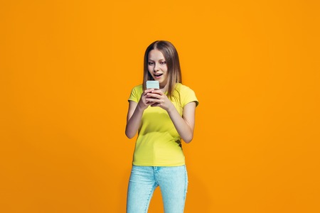 The happy teen girl standing and smiling against orange background.