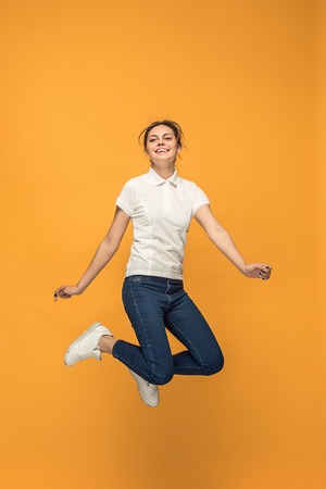 Freedom in moving. Pretty young woman jumping against orange background