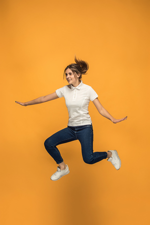 Freedom in moving. Pretty young woman jumping against orange backgroundの写真素材