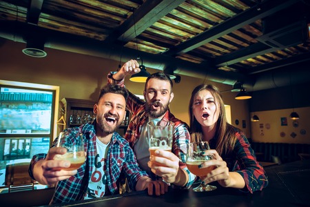 Sport, people, leisure, friendship and entertainment concept - happy football fans or male friends drinking beer and celebrating victory at bar or pubの写真素材