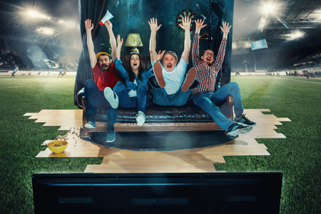 Soccer football fans sitting on the sofa and watching TV in the middle of a football field.の写真素材