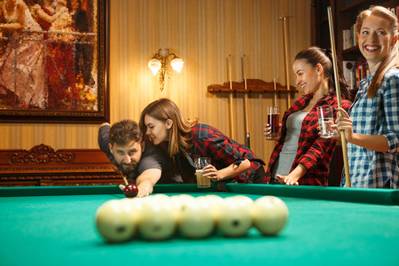Young men and women playing billiards at office after work.