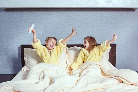 Happy laughing kids, boy and girl in soft bathrobe after bath play on white bedの写真素材