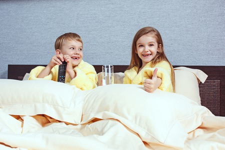 Happy laughing kids, boy and girl in soft bathrobe after bath play on white bedの写真素材