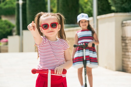 Preschooler girls riding scooter outdoors.