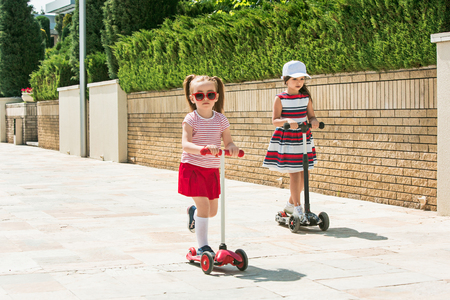 Preschooler girls riding scooter outdoors.の写真素材