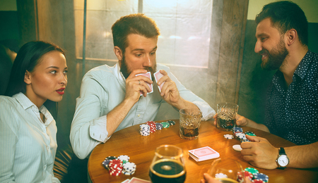 Side view photo of friends sitting at wooden table. Friends having fun while playing board game.