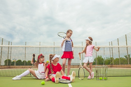 Portrait of group of girls as tennis players holding tennis racket against green grass of outdoor courtの写真素材
