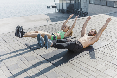 Fit fitness woman and man doing fitness exercises outdoors at cityの写真素材
