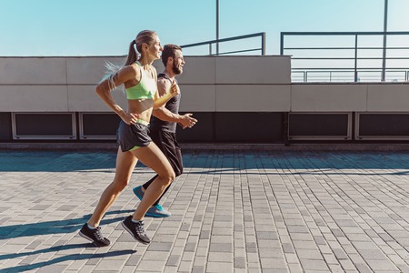 Pretty sporty woman and man jogging at city