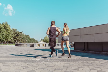 Pretty sporty woman and man jogging at city