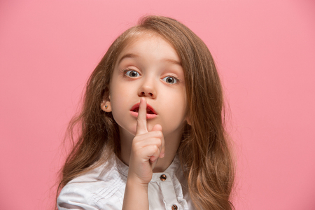 The young teen girl whispering a secret behind her hand over pink backgroundの写真素材