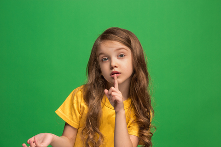 The young teen girl whispering a secret behind her hand over green backgroundの写真素材