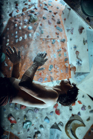 Free climber young man climbing artificial boulder indoors