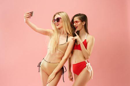 Cute girls in swimsuits posing at studio. Summer portrait caucasian teenagers on pink background.の写真素材