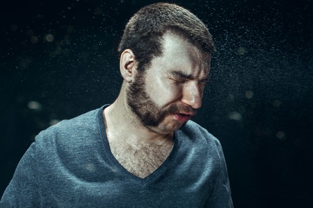 Young handsome man with beard sneezing, studio portraitの写真素材