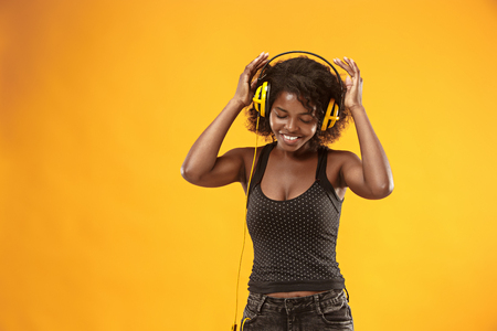 Studio portrait of adorable curly girl happy smiling during photoshoot. Stunning african woman with light-brown skin relaxing in headphonesの写真素材
