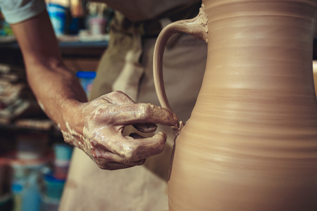 Creating a jar or vase of white clay close-up. Master crock. Man hands making clay jug macro.の写真素材