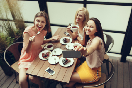 Two girl friends spend time together drinking coffee in the cafe, having breakfast and dessert.の写真素材