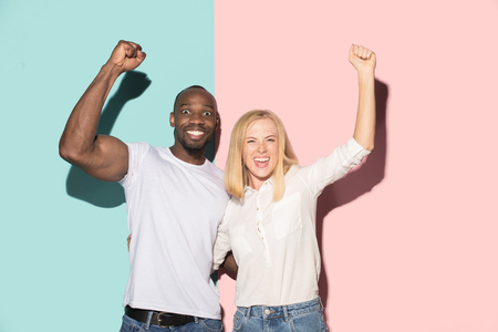 We won. Winning success happy afro man and woman celebrating being a winner. Dynamic image of caucasian female and male model on pink studio.の写真素材
