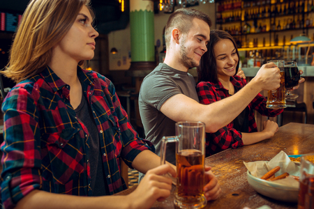people, leisure, friendship and communication concept - happy friends drinking beer, talking and clinking glasses at bar or pubの写真素材