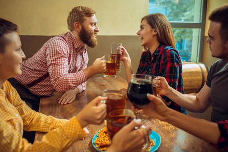 people, leisure, friendship and communication concept - happy friends drinking beer, talking and...